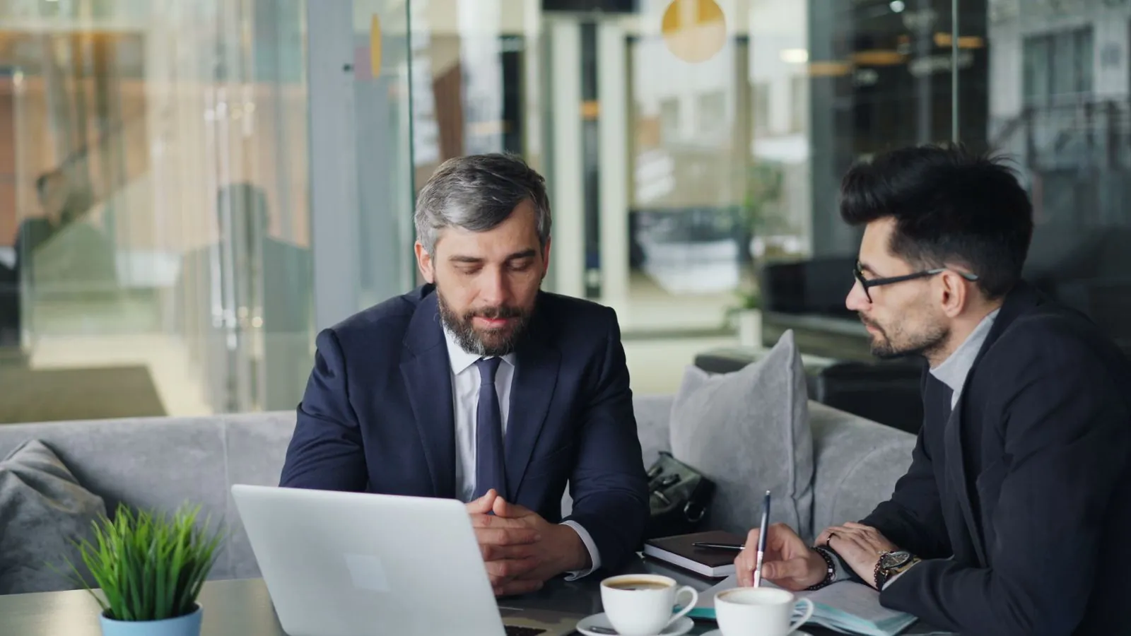 Two people in an office having a focused one on one conversation across a small table, one gesturing while the other listens.