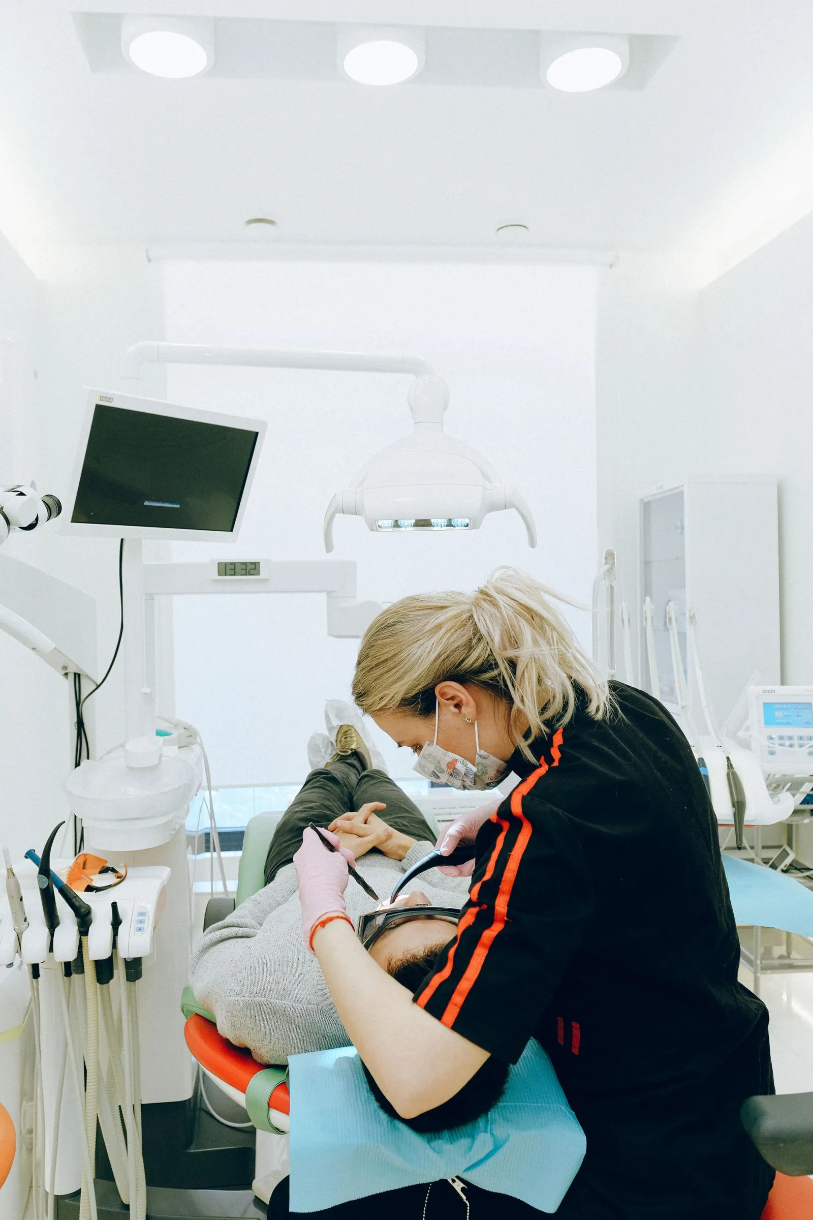 A dental hygienist in a professional office works carefully on a patient reclined in a bright dental chair.
