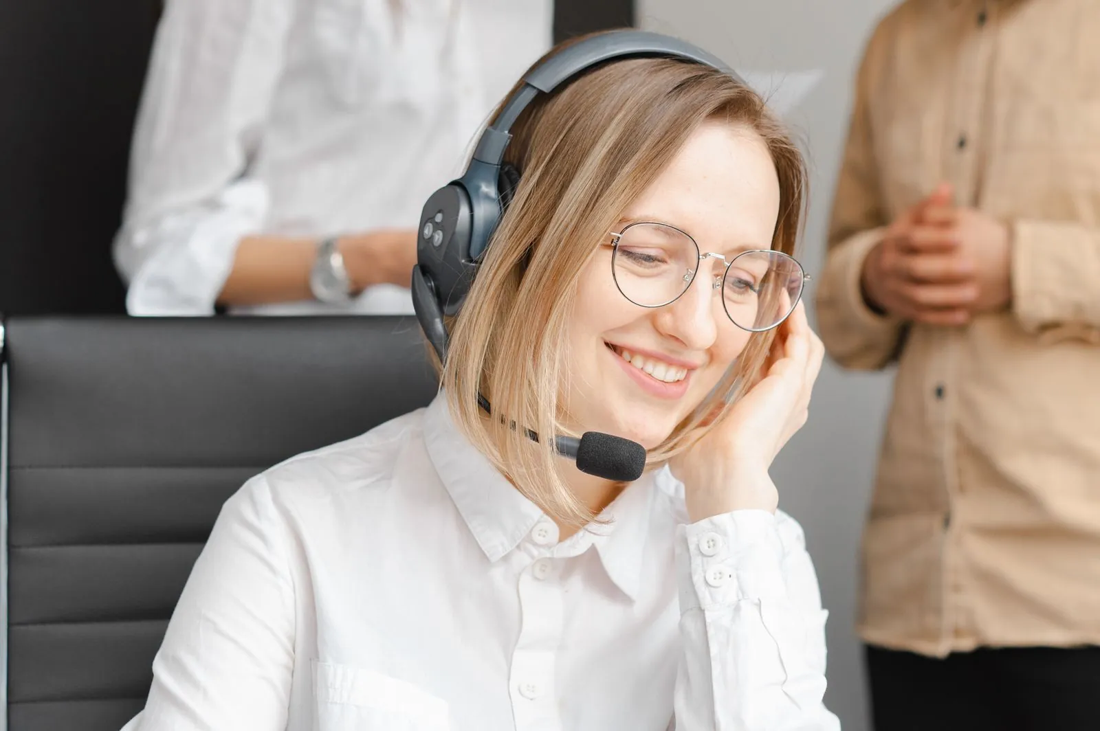 A friendly customer service specialist wearing a headset leans forward, listening intently to a question from a client.