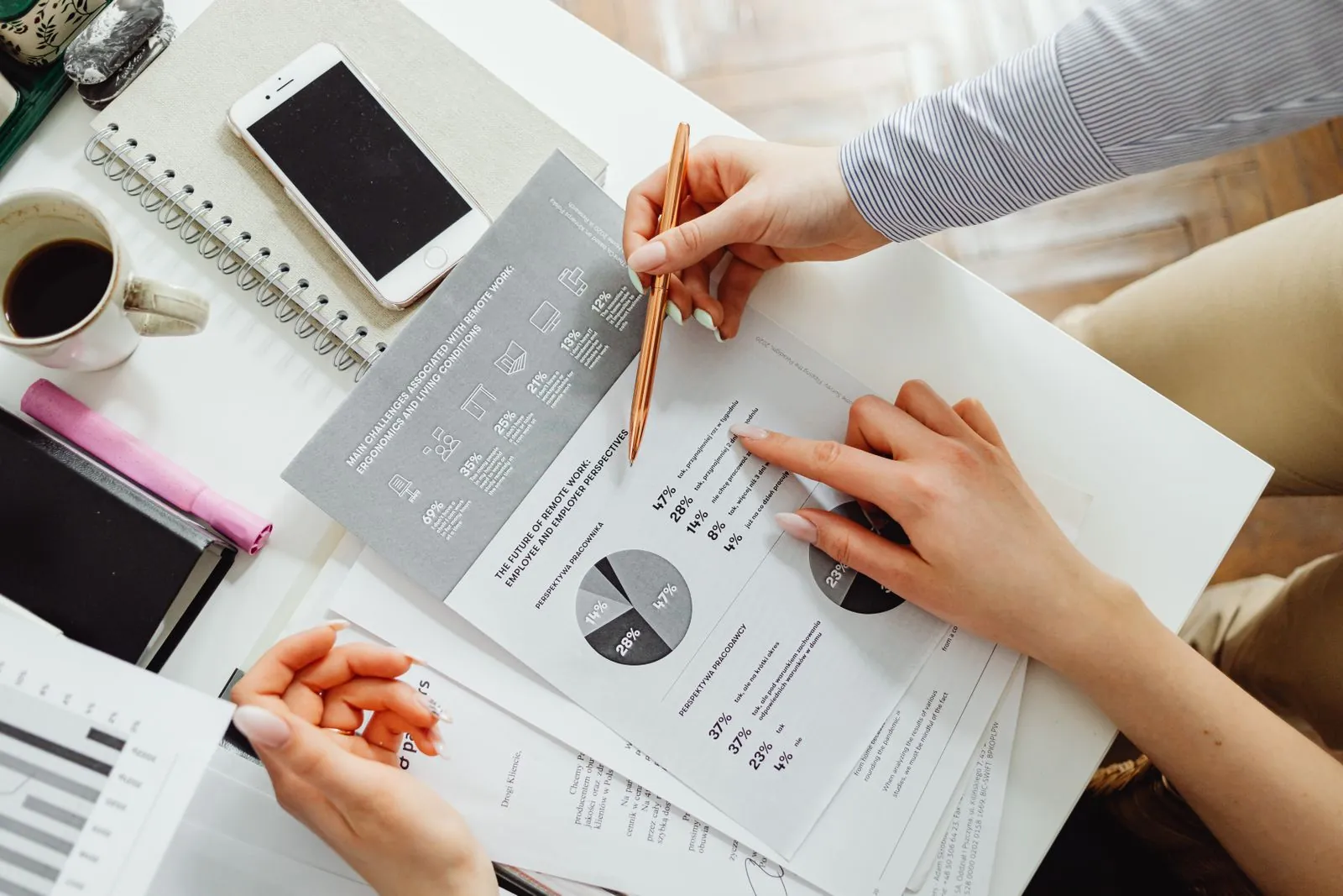 Two colleagues at a desk study a printed chart and a laptop showing a plan comparison, pointing at figures.