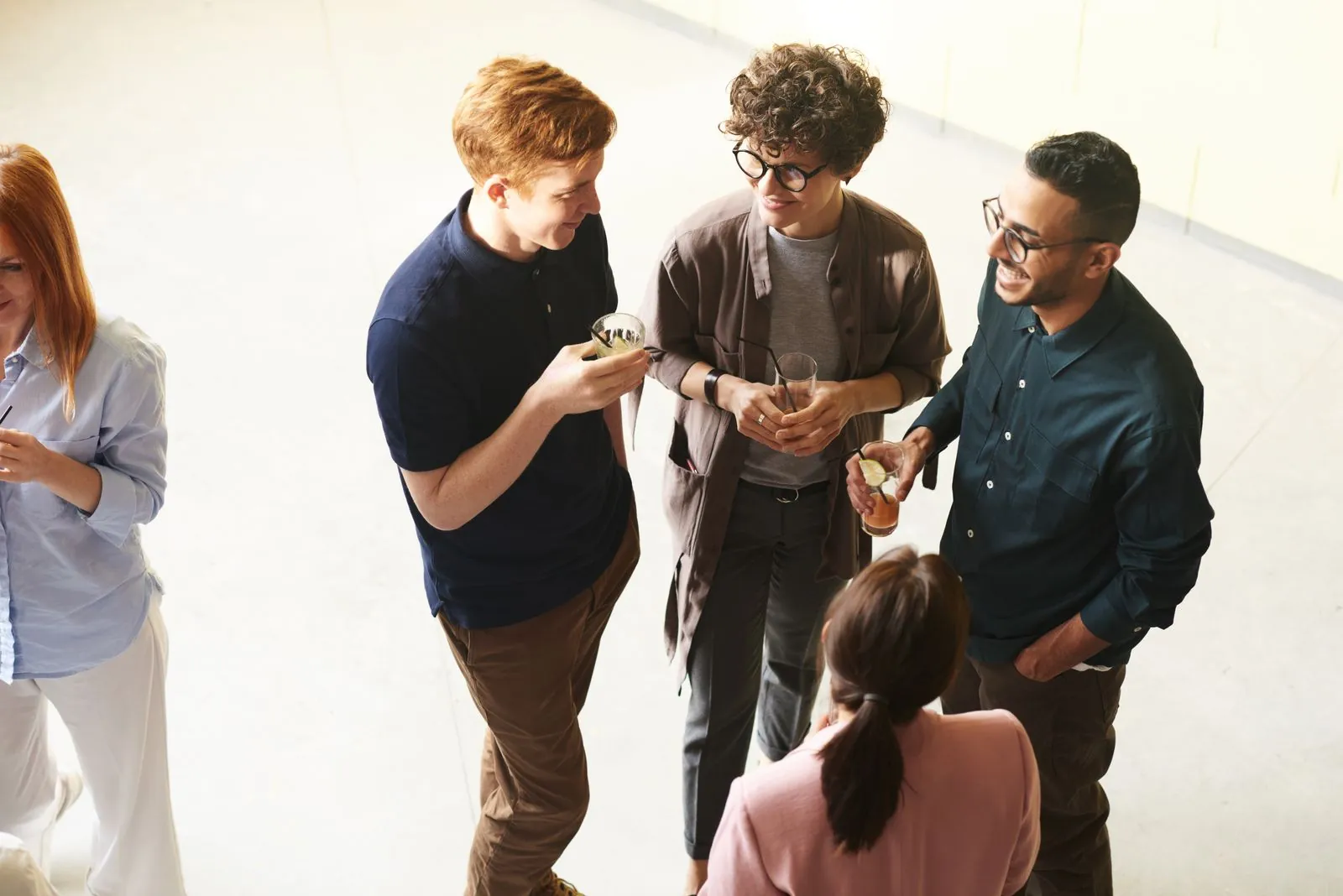 A group of young friends stand chatting and laughing together, holding drinks in a bright, airy loft.